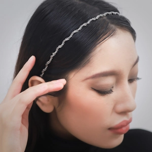 Elegant wavy silver bridal headband with pearl accents worn on dark hair against grey background