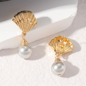 Boucles d'oreilles coquillage dorées avec perles sur fond de pierre blanche