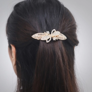 Barrette papillon dorée avec strass portée sur de longs cheveux bruns ondulés