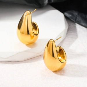 Vue détaillée de boucles d'oreilles gouttes dorées polies sur un support minimaliste