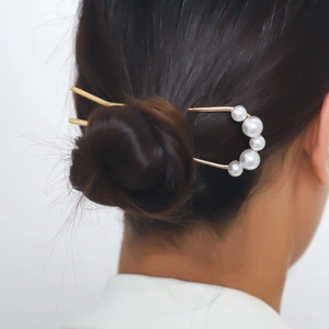 Detail showing the elegant U-shaped hair pin with pearls worn in a bun hairstyle