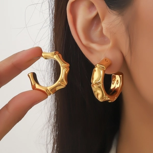 Gros plan de boucles d'oreilles créoles dorées en forme de bambou avec texture métallique