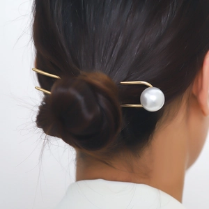 Close-up of elegant gold U-shaped hair pin with a large white pearl in dark hair
