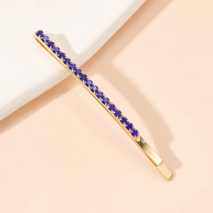 Détail d'une élégante pince à cheveux dorée ornée de strass bleu marine sur pierre blanche