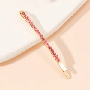 Détail d'une barrette dorée ornée de strass roses sur un support en marbre