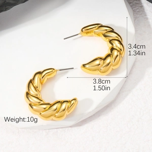 Vue macro détaillée de créoles dorées style croissant sur un plateau géométrique blanc