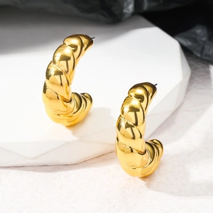 Détail de boucles d'oreilles créoles torsadées dorées sur un présentoir en marbre