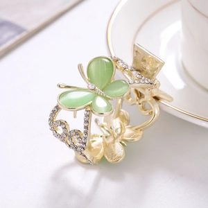 Eleganter Gold-Schmetterling-Haarclip mit grünen Steinen und Strass auf weißem Teller