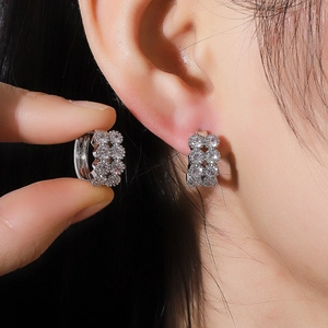 U-shaped silver hoop earrings with clear zircon stones shown on ear and held by fingers
