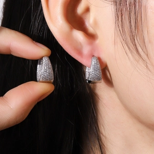Boucles d'oreilles géométriques en U argentées avec zircons portées sur l'oreille