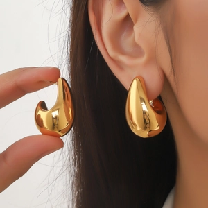 Élégantes boucles d'oreilles goutte dorées avec finition miroir portées par modèle