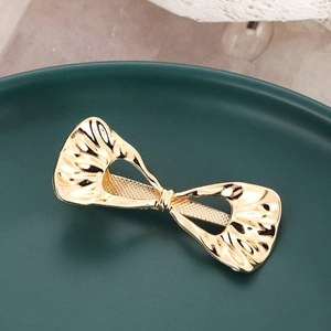 Barrette à cheveux nœud doré irrégulier avec texture ondulée sur assiette verte