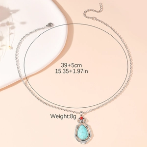 Boheemse zilveren druppelketting met turquoise steen en rode kraal op een roze achtergrond