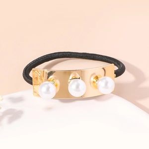 Détail d'un élastique à cheveux doré avec trois perles blanches et ruban noir souple
