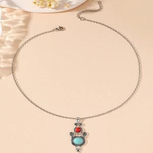 Collar bohemio de plata con piedra turquesa ovalada y cuenta roja sobre fondo beige