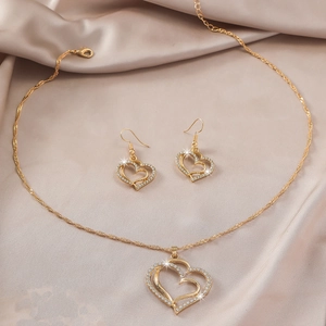 Detailed shot of golden hollow heart jewelry set with rhinestones on silk background