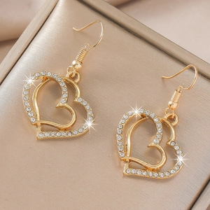 Detailed close-up of golden heart drop earrings with sparkling rhinestones on silk