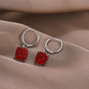 Elegant silver hoop earrings with square red crystal charms on dark silk background