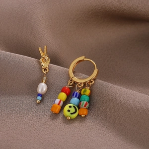 Macro shot of asymmetric earrings with smiley beads and gold peace gesture on brown velvet
