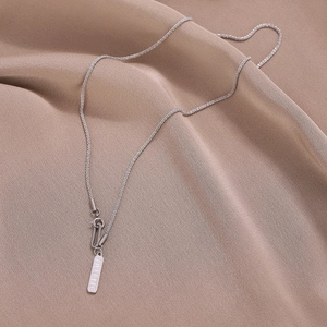 Minimalist silver fillette necklace with rectangle pendant on pink fabric background