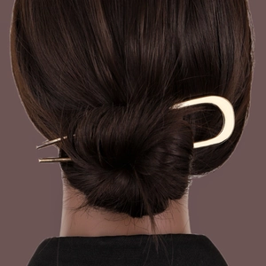 Minimalist gold U-shaped metal hair pin with enamel detail on a sleek bun hairstyle