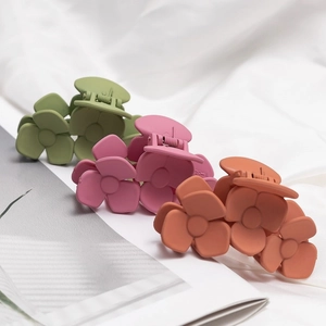 Trois pinces à cheveux fleurs mates en vert et rose sur un fond de tissu blanc doux