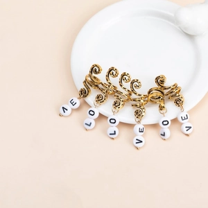 Vintage gold metal dreadlock rings set with LOVE letter beads on white ceramic tray