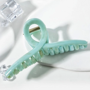 Macro detail of mint green hair claw with marble texture and gold metal spring