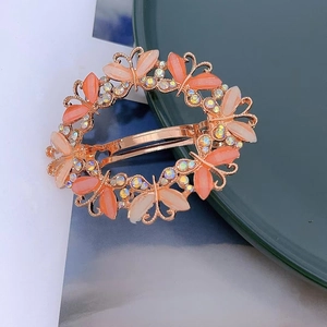 Close-up of elegant rose gold hair clip with orange butterfly wreath and small rhinestones
