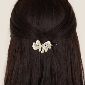 Pince à cheveux nœud dorée avec strass blancs portée sur de longs cheveux bruns
