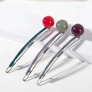 Three minimalist hair clips with red green and purple balls on white geometric stands