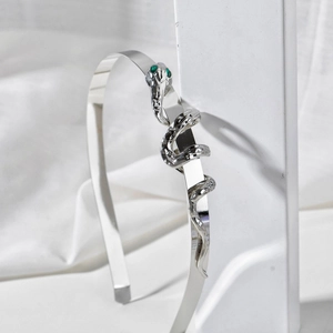 Polished silver metal snake headband with green gemstone eyes on a white minimal setup