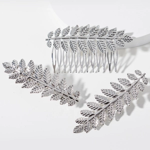 Silver metal hair comb and clips set with detailed hollow leaf design on a white platform