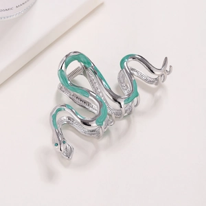 Silver snake hair claw clip with green enamel finish and emerald gemstone eyes on beige background