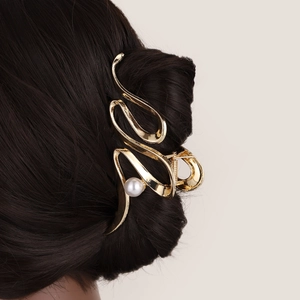 Close-up of golden wave metal hair claw clip with a white pearl on long dark hair