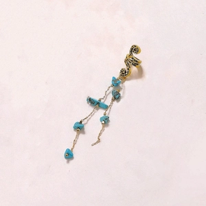 Détail du bijou d'oreille serpent doré avec pendentifs en pierres de turquoise