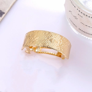 Macro shot of gold alloy hair clip with brushed texture and ergonomic curved metal design