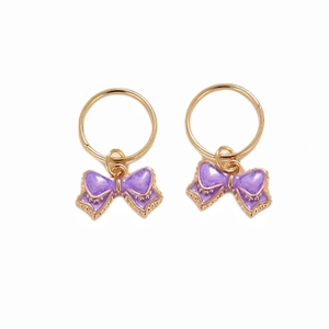 Detailed close-up of golden metal rings featuring purple enamel bow charms for hair and jewelry