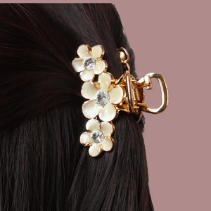 Pince à cheveux dorée avec trois fleurs en émail blanc et cristaux sur cheveux noirs