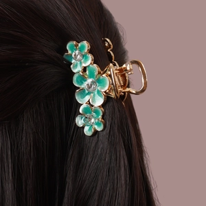 Détail d'une pince à cheveux dorée avec trois fleurs en émail vert et strass brillants