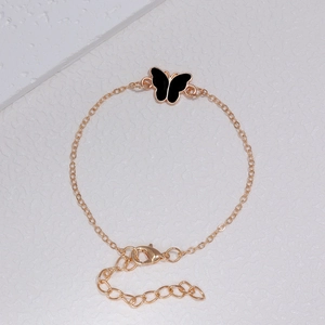 Detail eines goldenen Armbands mit schwarzem Emaille-Schmetterling und Karabinerverschluss