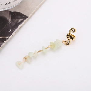 Détail d'un ear cuff doré en spirale avec pierres naturelles vertes sur fond blanc
