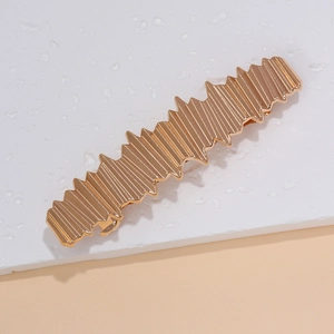 Détail d'une pince à cheveux dorée avec rayures verticales et bords zigzag unique