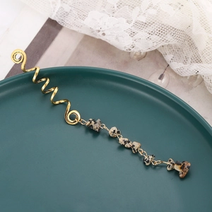 Close-up of golden spiral hair charms with natural spotted stone pendants on lace