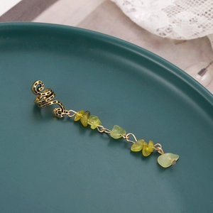 Detailed macro view of vintage gold alloy ear cuff with light green stone tassel