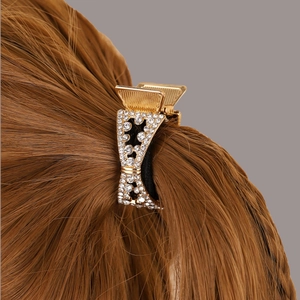 Detail of a gold-toned metal hair claw clip with sparkling rhinestones on brown hair