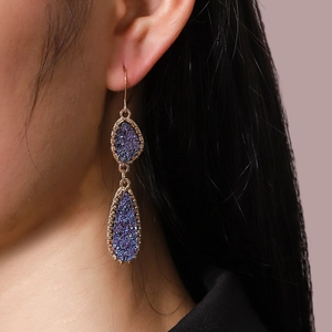 Détail des boucles d'oreilles double goutte violettes avec bordure perlée dorée sur modèle