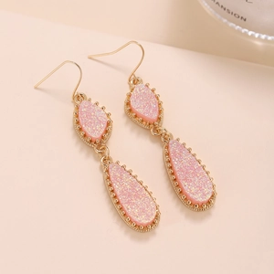 Vue détaillée de boucles d'oreilles en cristal de résine rose avec bordures dorées texturées