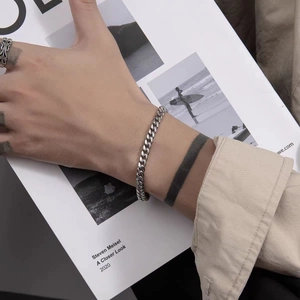 Close-up of a silver Cuban link bracelet on male wrist with vintage ring and magazine background