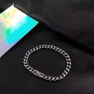 Macro detail of silver stainless steel Cuban link bracelet with square clasp on black leather